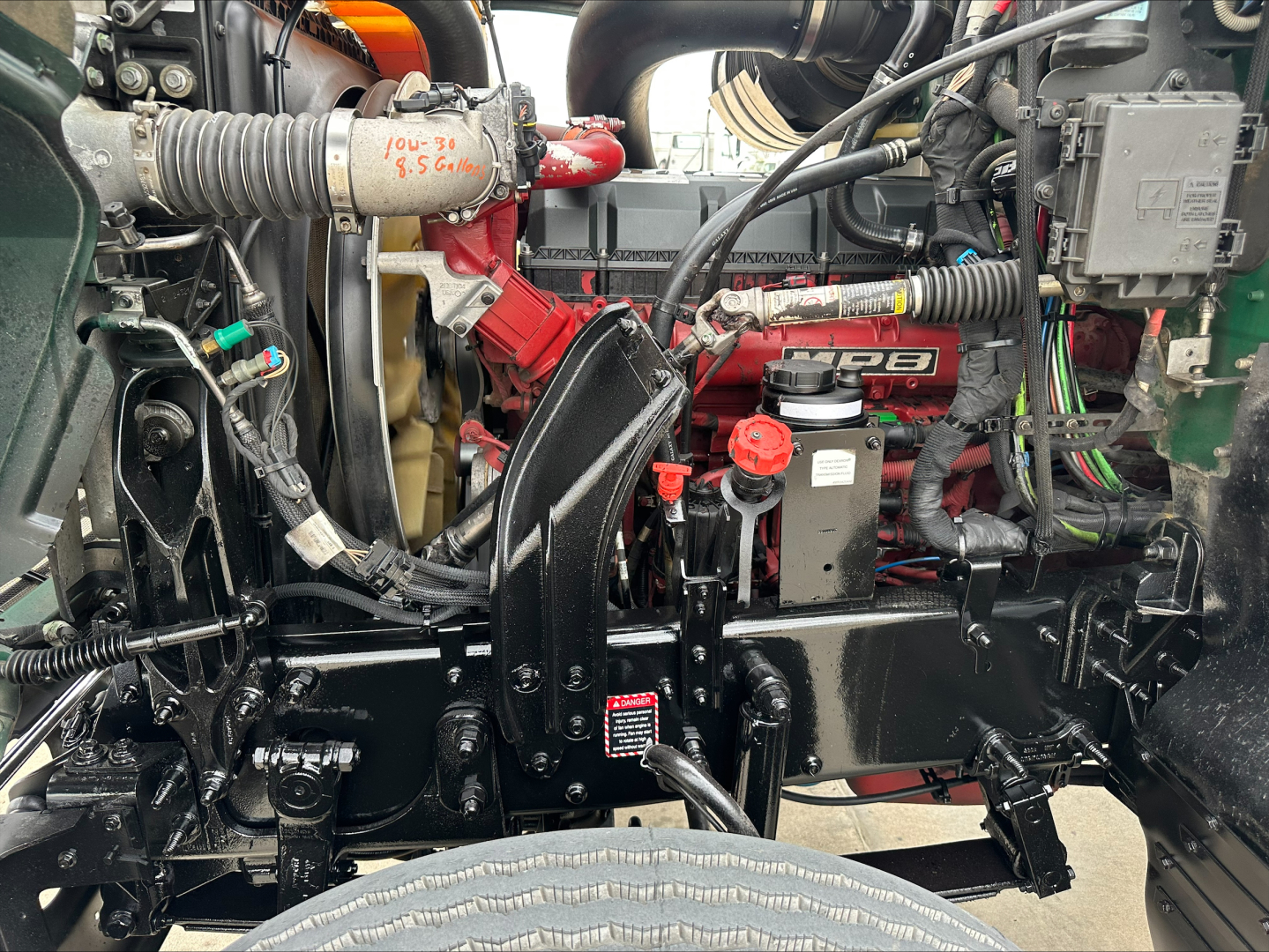 Mack PI64T engine bay showing diesel engine with red components, cooling hoses, wiring, and front suspension in view.