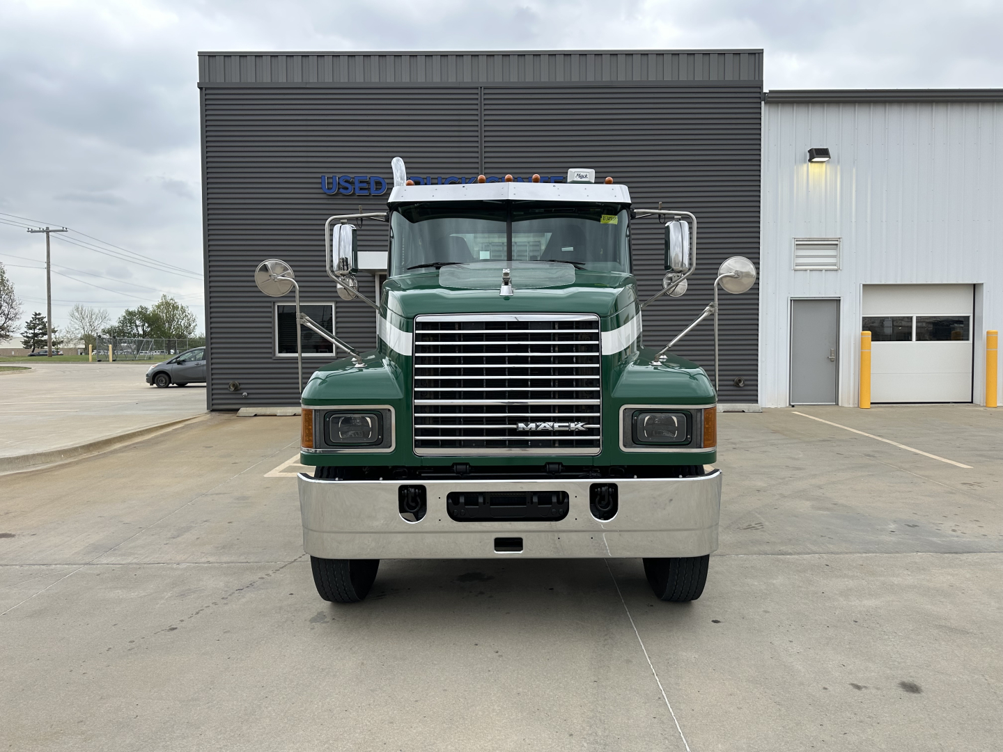 Mack PI64T conventional daycab front view showing large chrome grille, green cab, bumper, and mirrors.