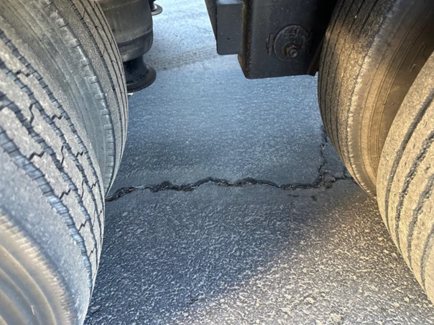 Dual rear trailer tires with a gap between them and visible asphalt surface.