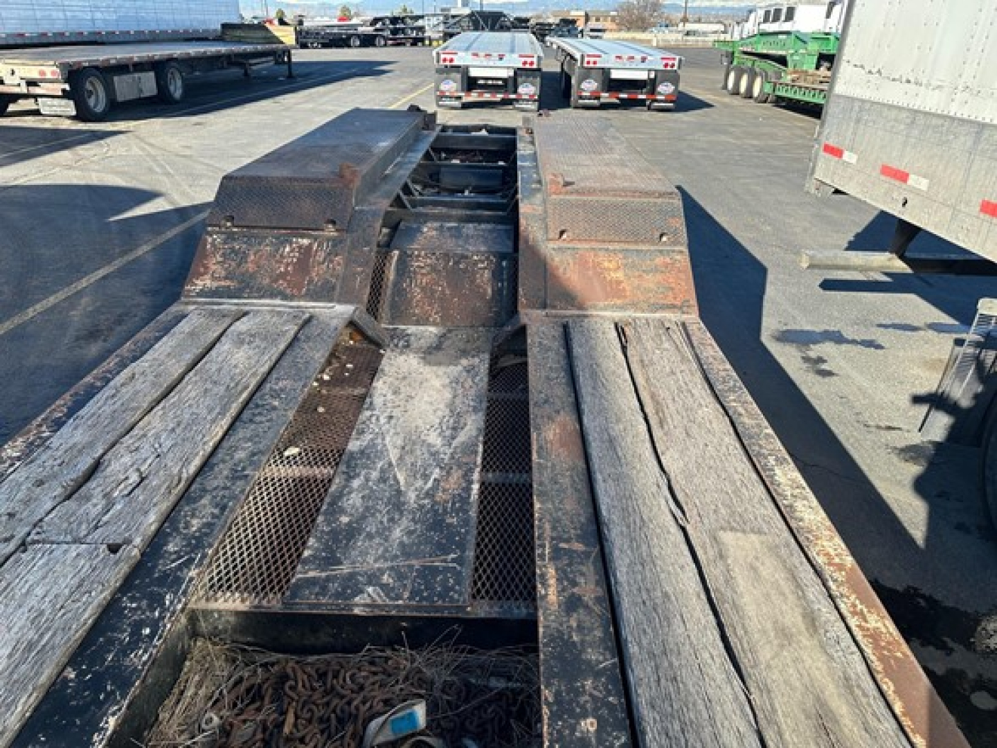 Lowboy trailer bed with steel plates and worn deck sections from a Load King 55 Ton trailer, visible rust, wheel wells, and kingpin area at the center of the bed.