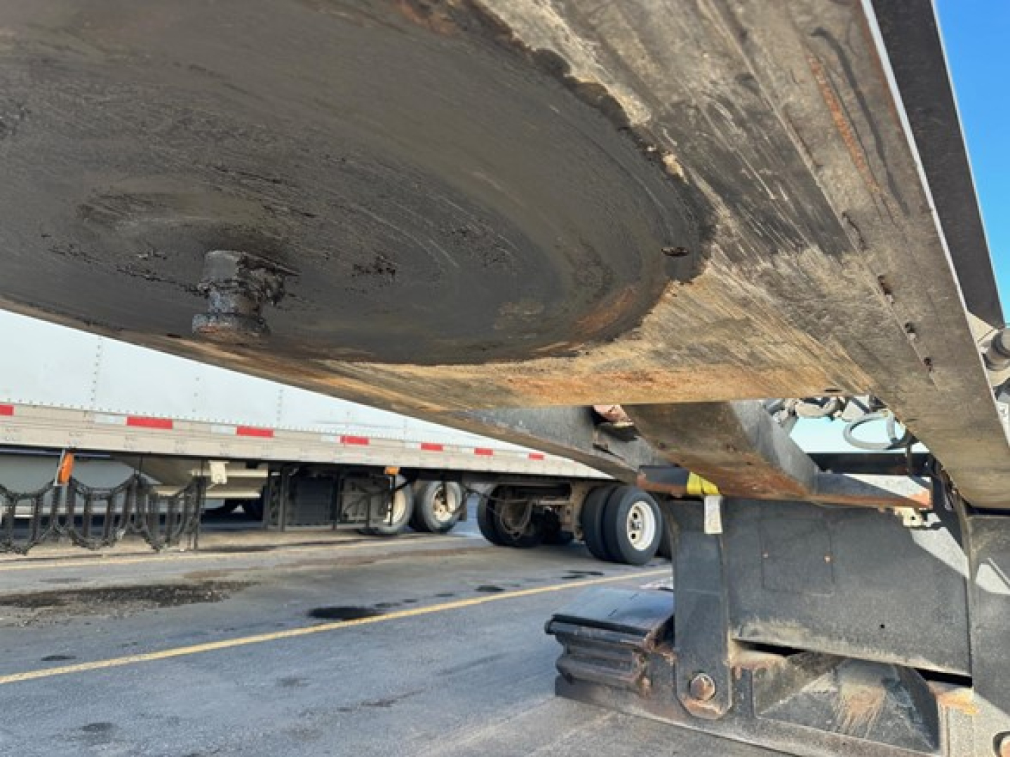 Lowboy trailer underside showing steel beam and support leg with dirt and grime visible undercarriage.