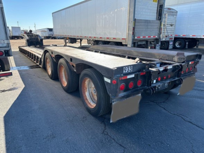 Lowboy trailer showing rear view with triple axles, black frame, and reflective lights.