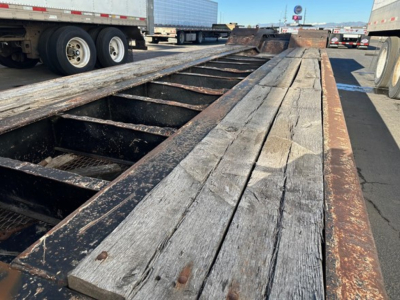 Lowboy trailer deck with weathered wooden boards and metal frame, long flatbed extending into distance, Load King 55 ton trailer in a yard.