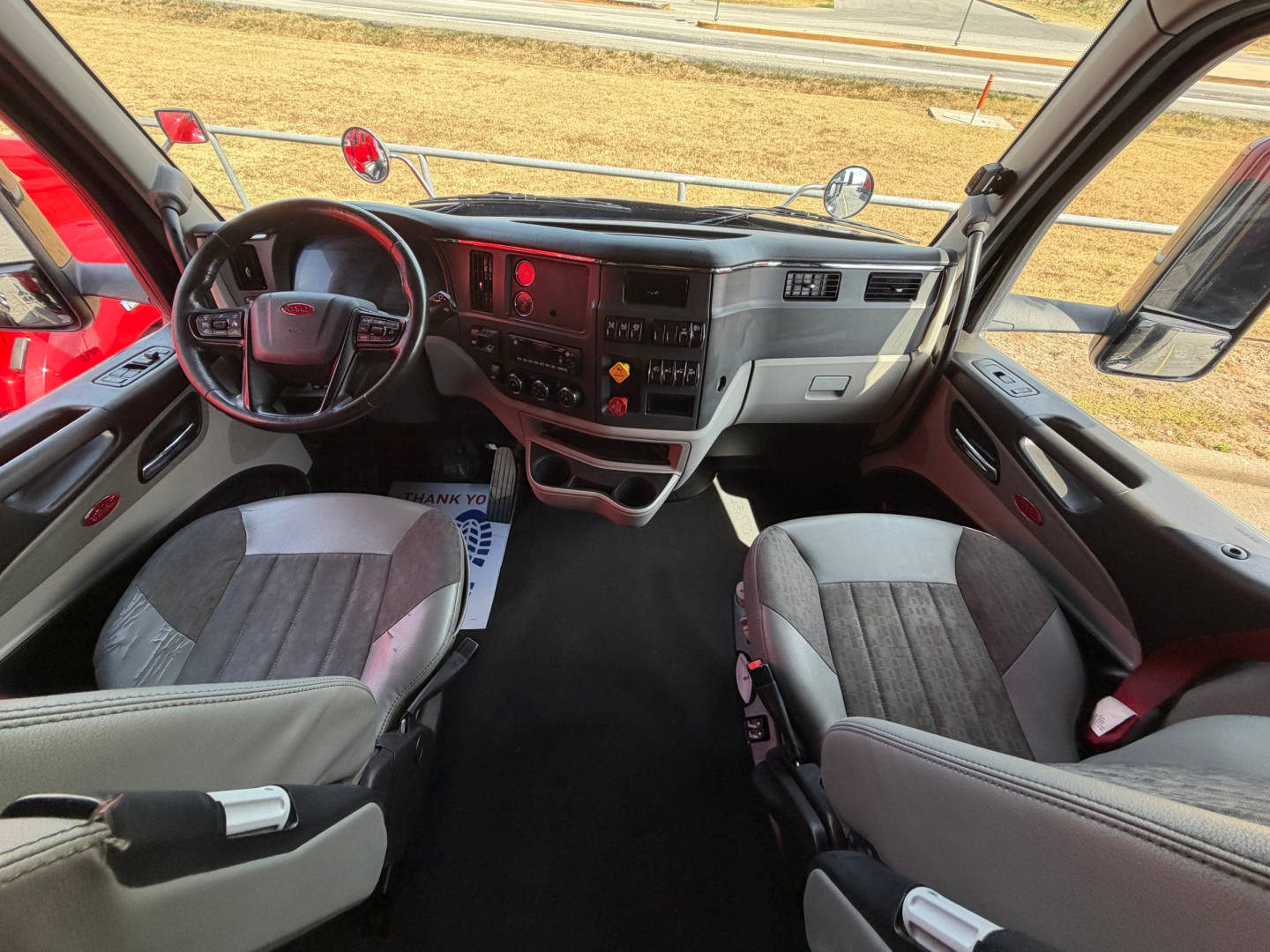 Interior of a 2022 Peterbilt 579 cab showing steering wheel, dashboard with digital screens, center console, and two front seats.