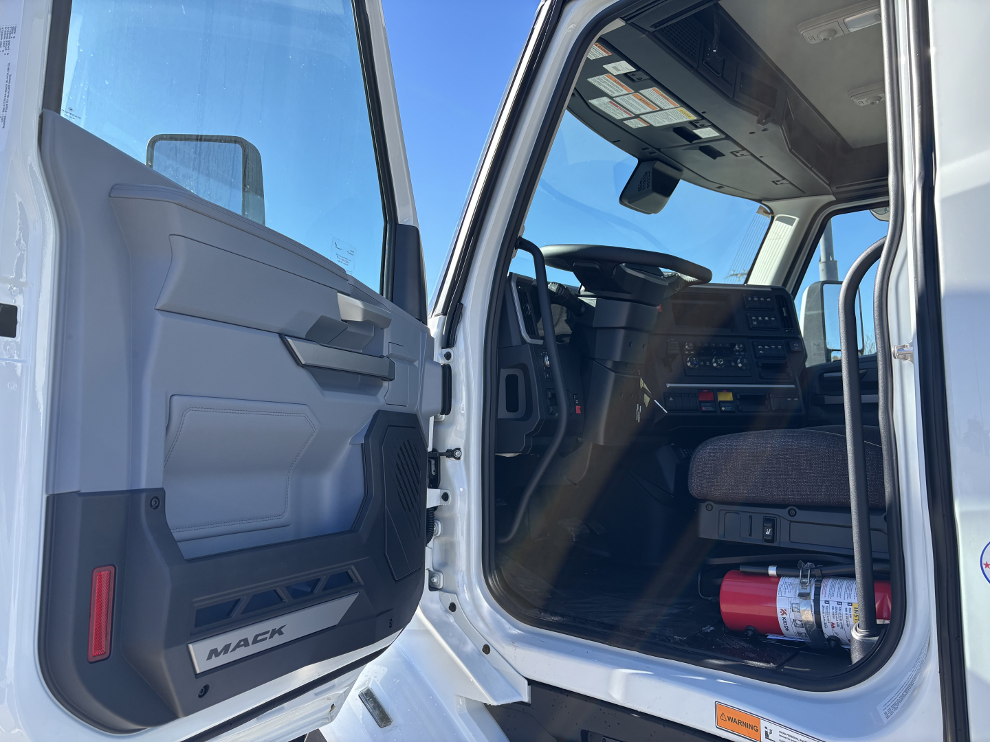 Mack PR64T cab interior and open driver door showing dashboard and steering wheel.