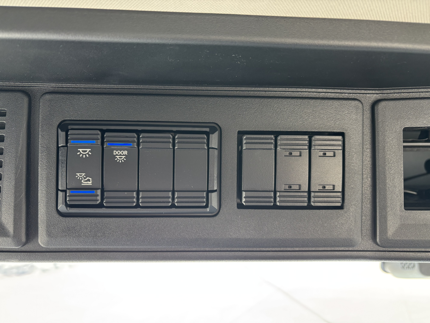 Dashboard control panel showing multiple switches and blue-illuminated symbol buttons in a Mack PR64T cab.