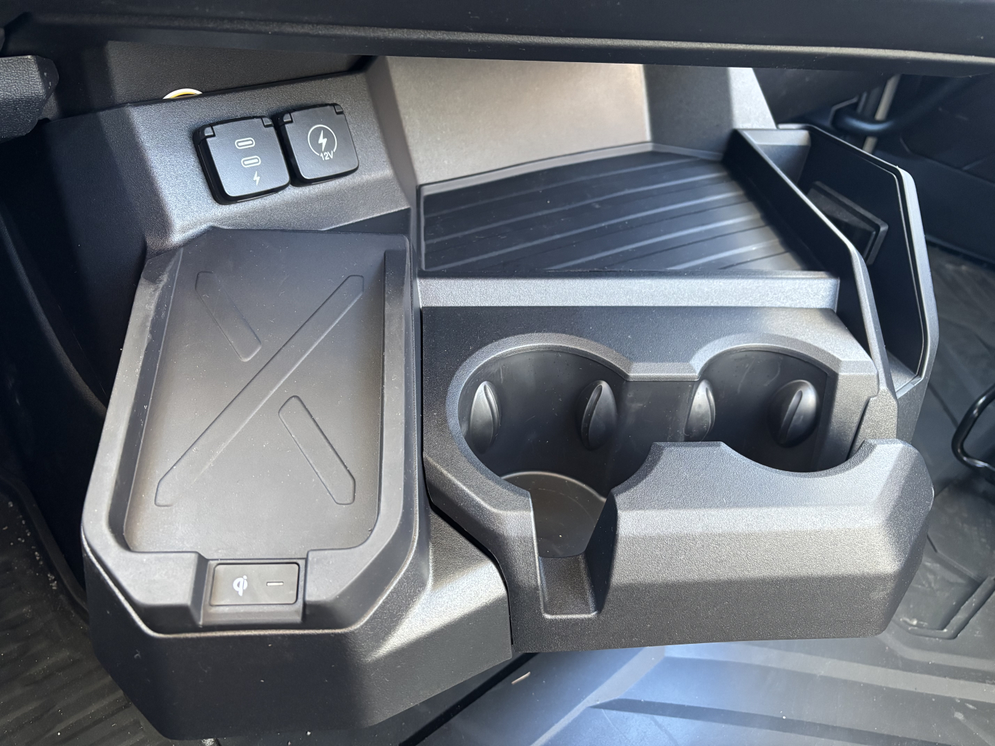 Interior center console with cup holders and storage area in a Mack PR64T truck cab showing cup holders and power/aux switches.