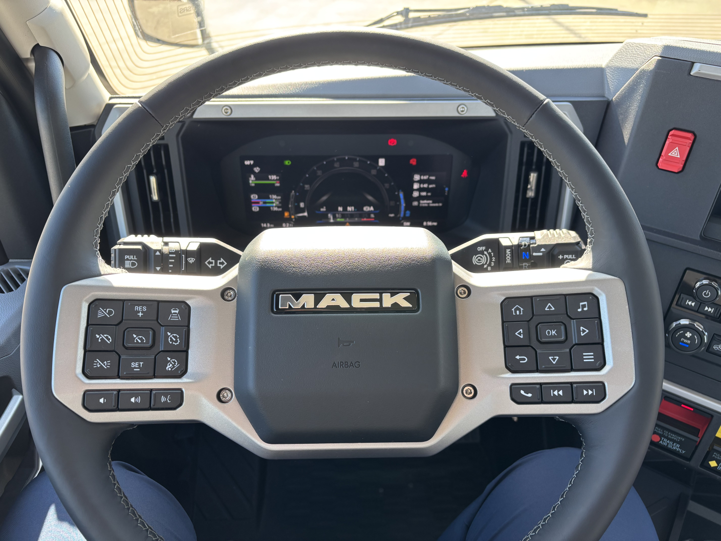 Mack PR64T truck interior showing steering wheel with Mack logo and digital instrument cluster.