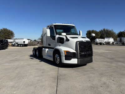 Mack PR64T conventional day cab truck front-left view with white cab and black grille in a lot.
