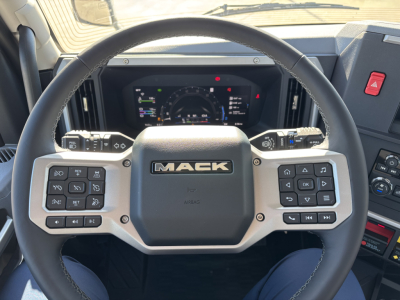 Mack PR64T truck interior showing steering wheel with Mack logo and digital instrument cluster.