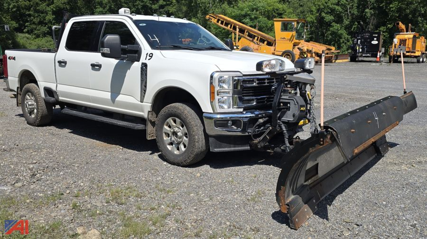 Ford F-350 Super Duty XLT Crew Cab pickup with plow attached, front view, white with grille guard, plow blade resting on ground.