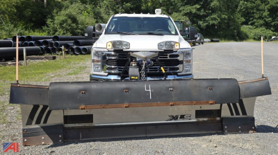 Front view of a 2023 Ford F-350 Super Duty XLT Crew Cab with a large plow attached, headlights on, in a gravel lot.
