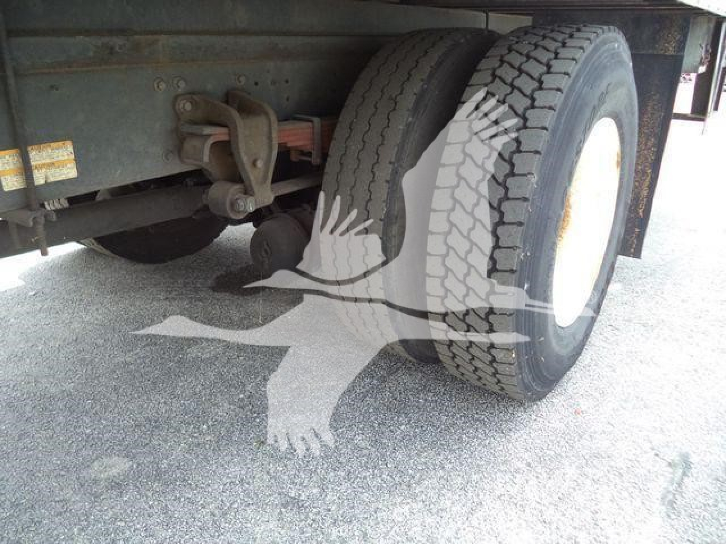 Truck rear axle area with dual wheels and white rims; chassis and leaf spring suspension visible under the refrigerated truck.