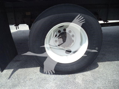 Wheel and tire of a refrigerated truck, white steel rim, tire tread visible, undercarriage and mudflap in background.