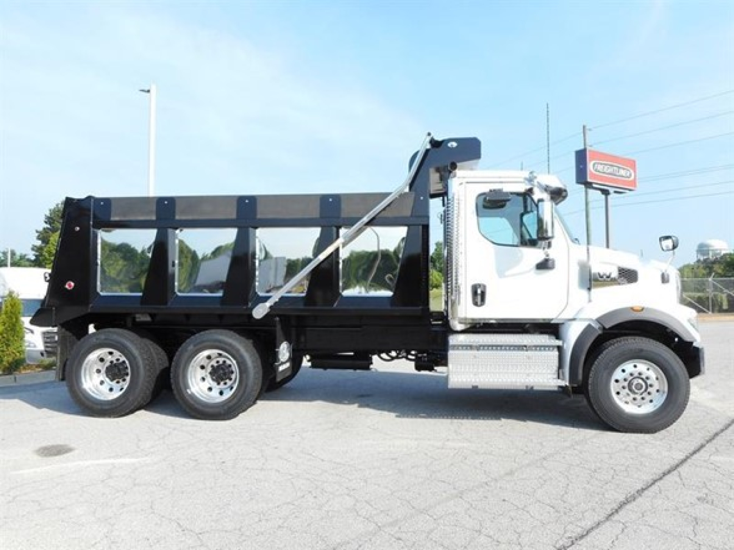 Dump truck with white cab and black dump body, side view showing 3-axle rear suspension, chrome steps, and logo on front door; no visible text on the vehicle itself.