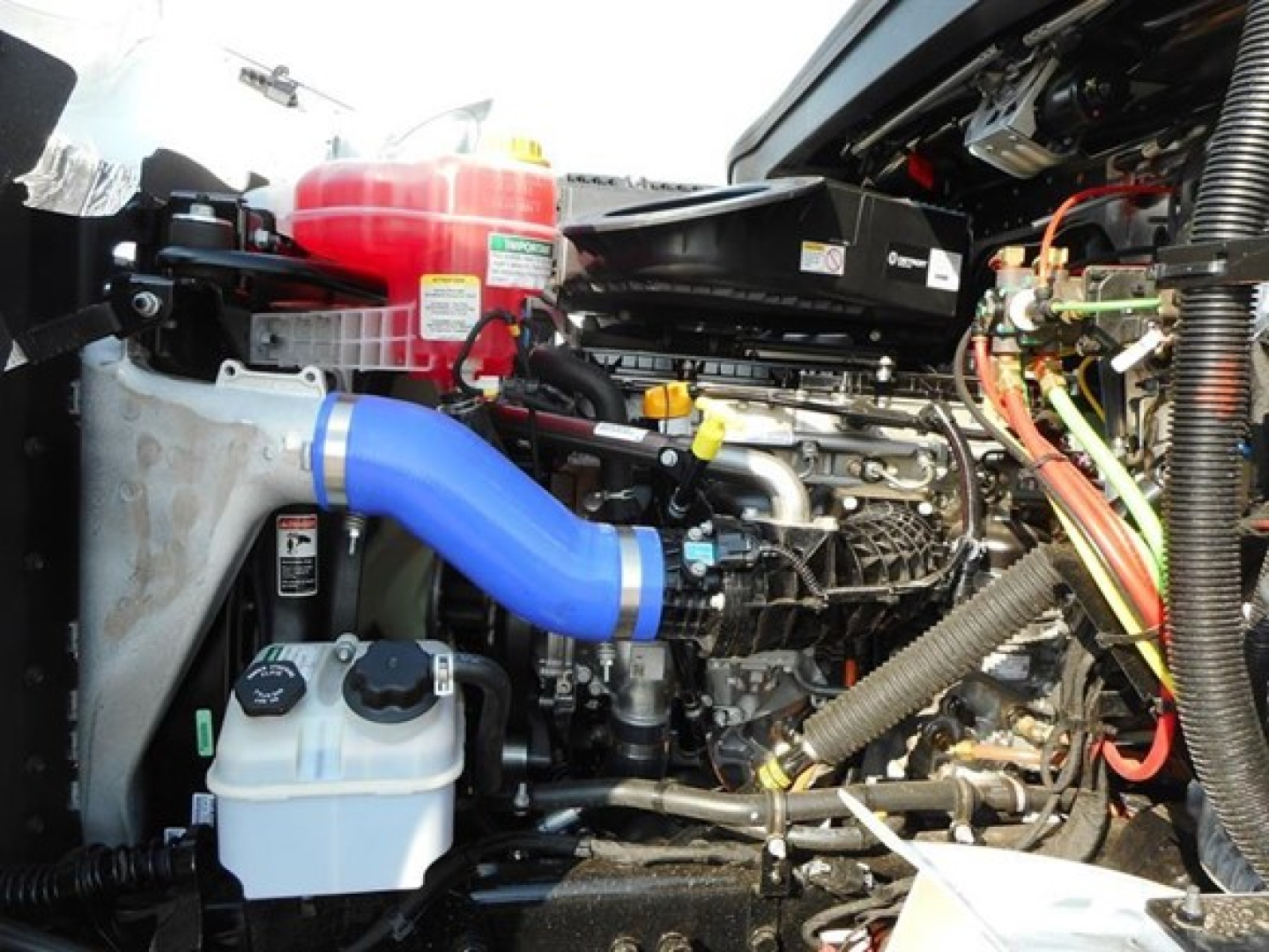 West Star 47X engine bay showing blue coolant hose, red coolant reservoir, white windshield washer reservoir, and various hoses and wiring in the engine compartment.