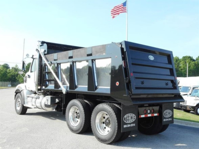 Dump truck rear angled view showing cargo bed, dual rear wheels, and black tailgate with GE logo; Western Star 47X branding not visible; flag in background