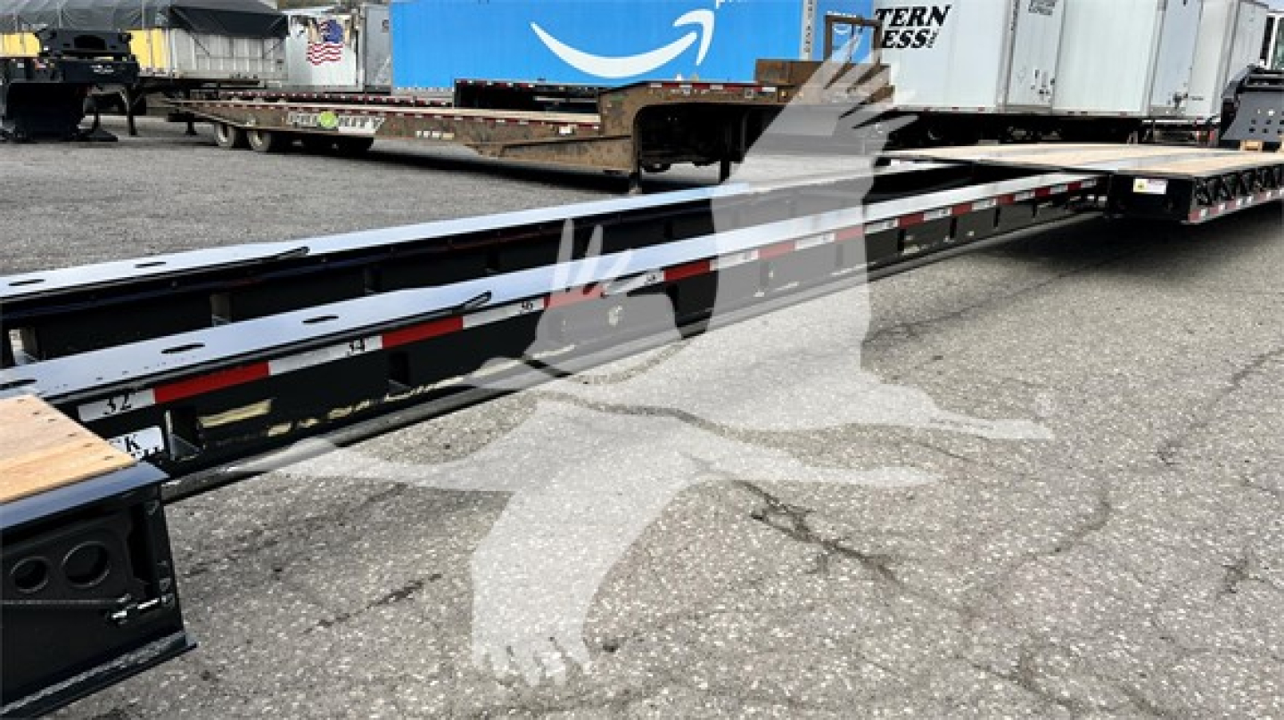 Long lowboy trailer deck showing metal frame and side rails with reflective red/white tape.
