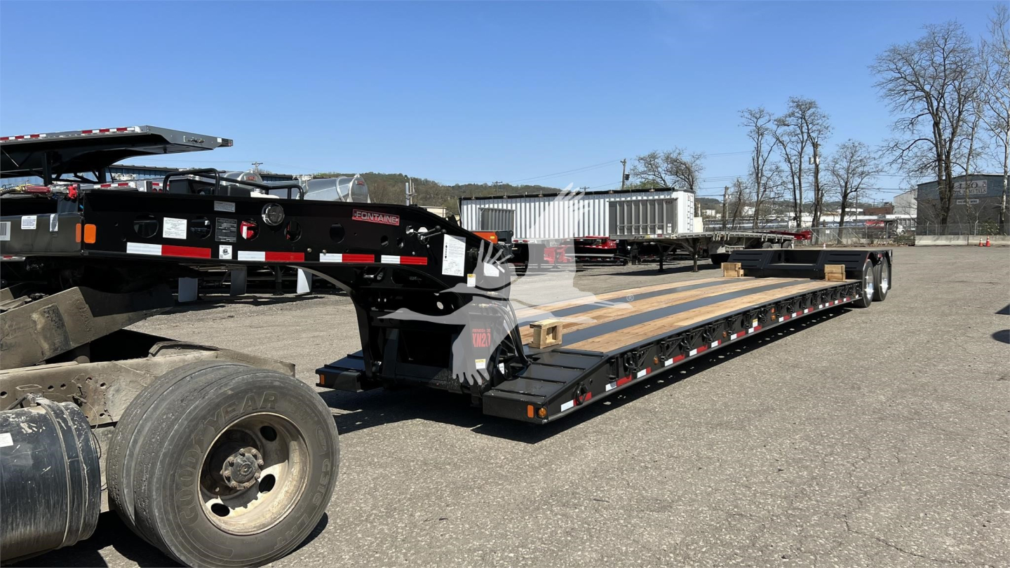 Long black Fontaine XN20 lowboy trailer with wood deck and multiple axles, docked in an outdoor lot.