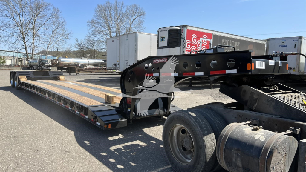 Fontaine XN20 lowboy trailer in view with long flatbed, black frame, ramps, and wheel area; visible decals and hitch components.