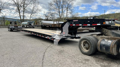 Large lowboy trailer with extended deck and black gooseneck, Fontaine XN20 logo visible, long steel frame, dual rear axle tires, equipment yard background.