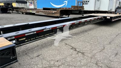Long lowboy trailer frame showing reflective safety stripes and side rails, with storage on top and other trailers in background.