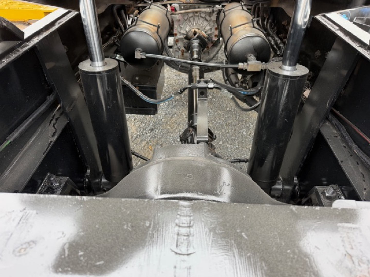 Truck chassis underside view showing dual air spring struts, driveshaft, and engine components between the rear frame rails.