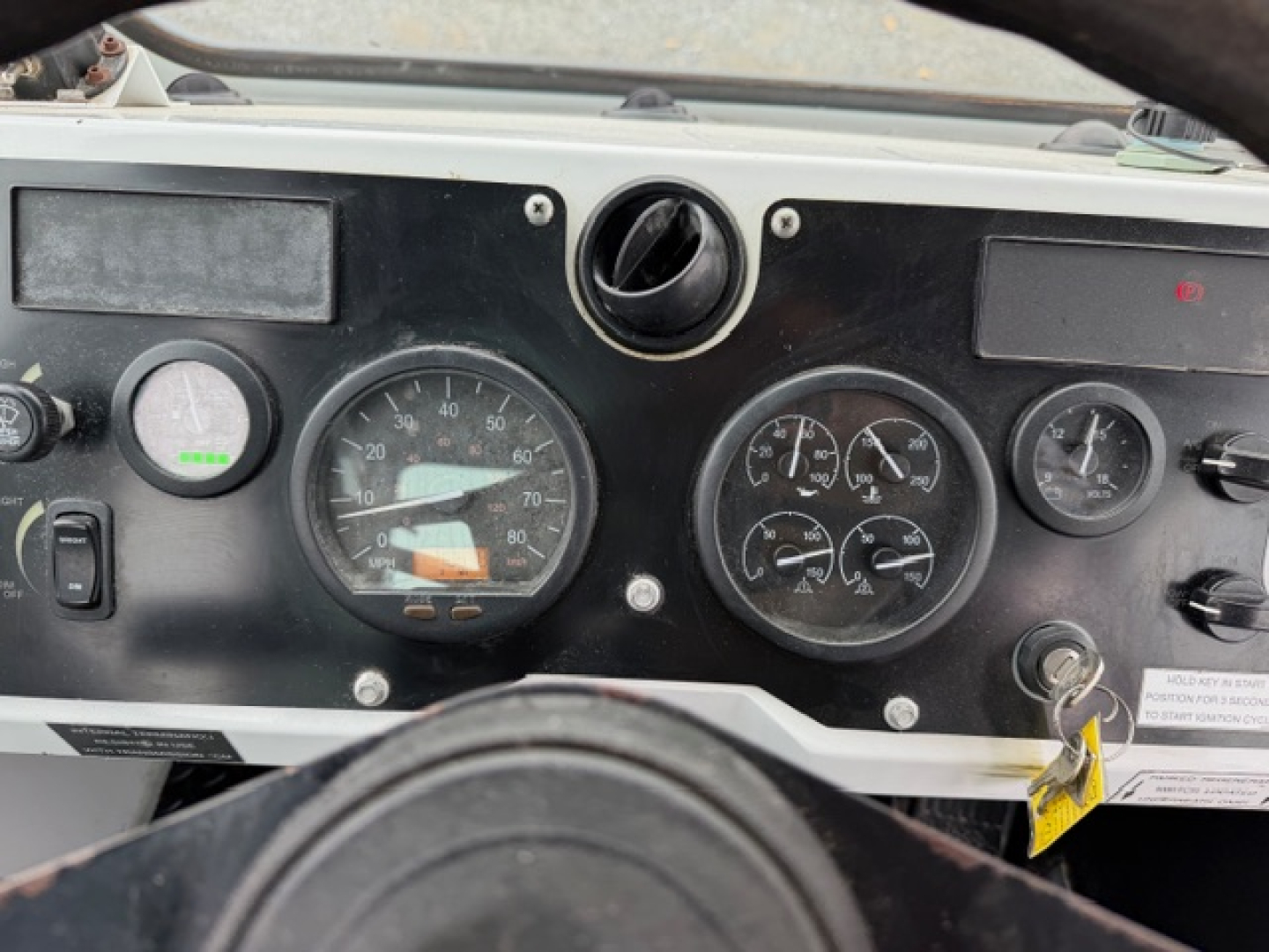 Dashboard of 2021 Capacity TJ5000 showing multiple gauges and steering wheel. Visible: large speedometer, tachometer, smaller gauges, ignition switch, and warning labels.