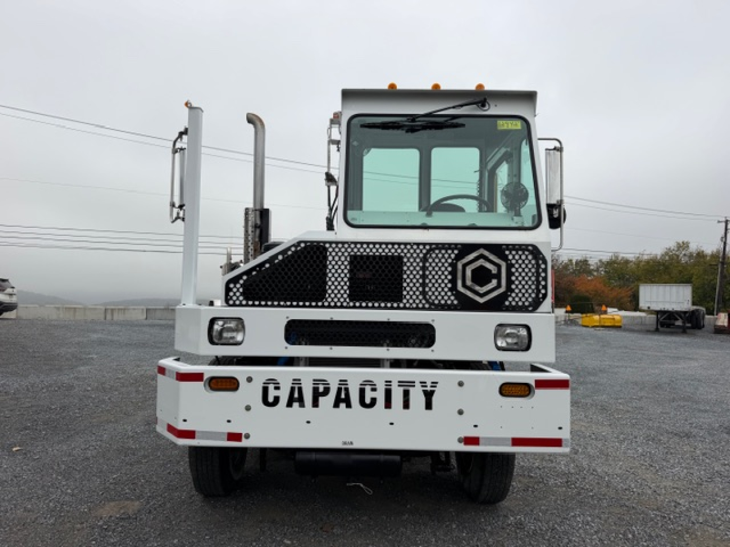 Front view of a white TJ5000 capacity truck with 'CAPACITY' on the grille and stock number label, showing cab, large windshield, and dual exhaust stacks.