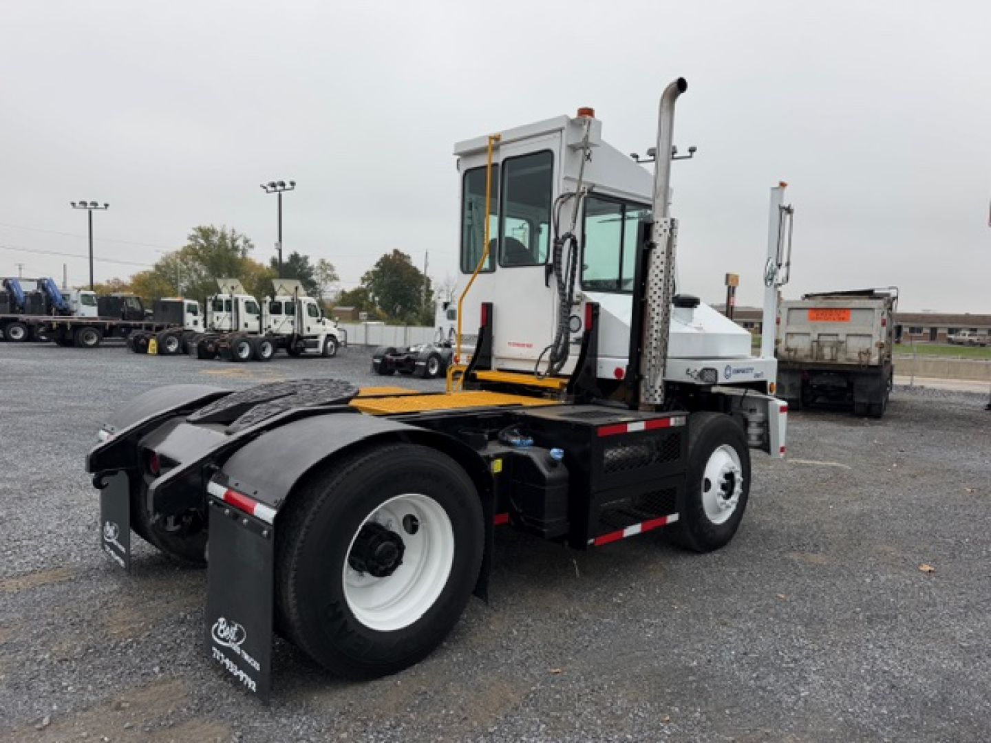 TJ5000 yard truck chassis with white cab, black frame, dual rear wheels, and vertical exhaust; visible sticker area and background showing other trucks.