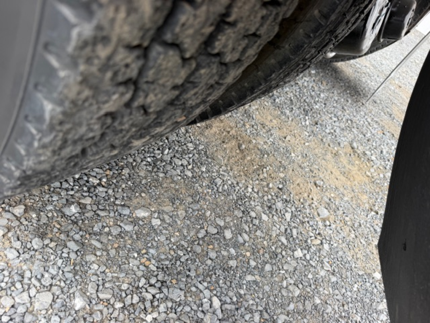 Truck wheel and tire tread visible under vehicle showing gravel ground surface.