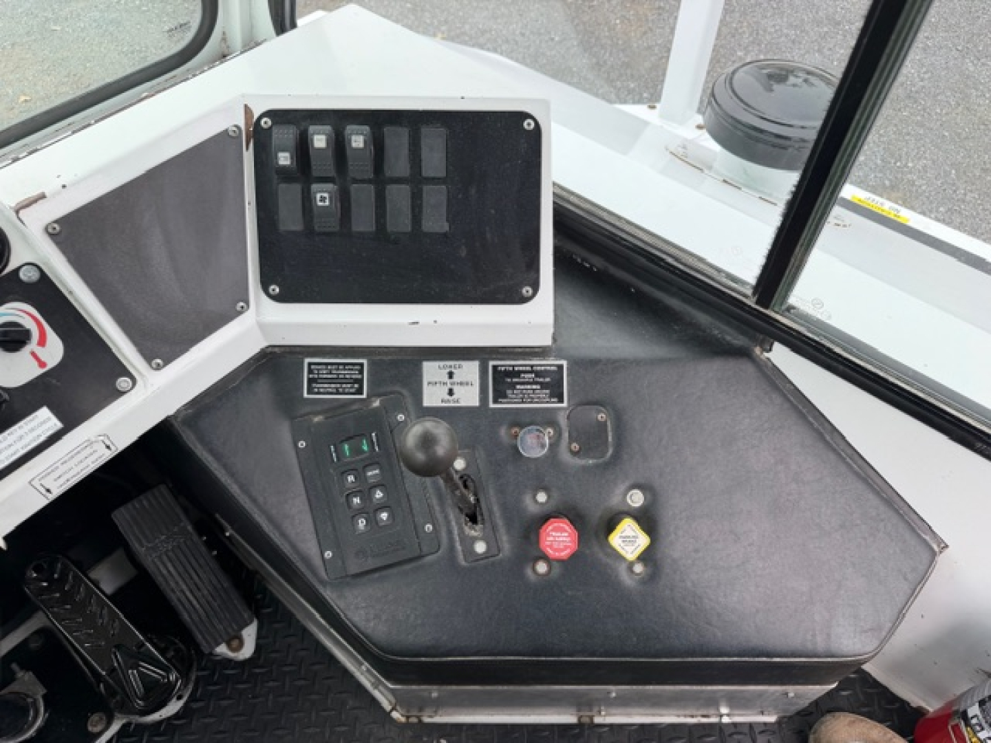 Control panel and drivers seat area of a TJ5000 crane/utility vehicle showing switches, key lock, red emergency stop, yellow caution button, and joystick lever.