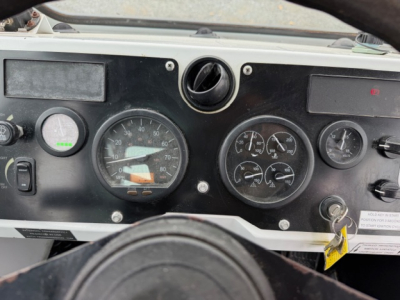 Dashboard of 2021 Capacity TJ5000 showing multiple gauges and steering wheel. Visible: large speedometer, tachometer, smaller gauges, ignition switch, and warning labels.