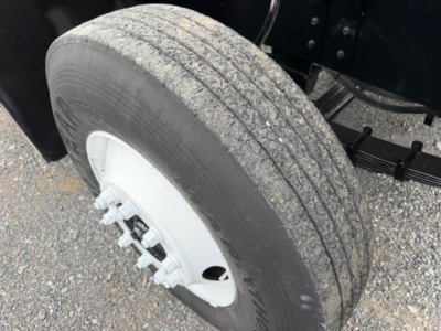 Truck wheel and tire with white steel rim showing lug nuts and part of axle assembly.
