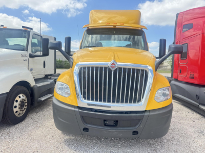Truck front view of a yellow 2019 International LT conventional daycab with large chrome grille and black bumper; side mirrors visible and other trucks in background.