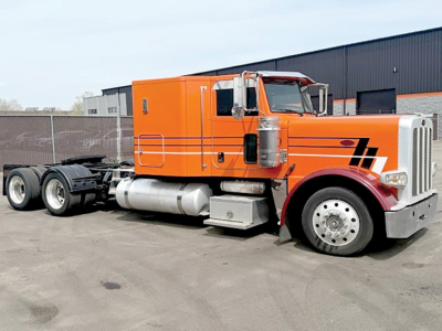 Orange Peterbilt 388 semi-truck tractor with sleeper cab, chrome bumper, side fuel tanks, and black and orange stripe graphics.