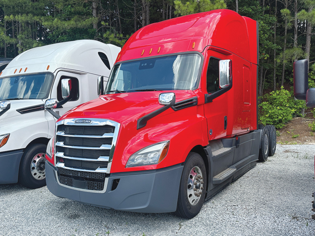 2024 Freightliner Cascadia126 tractor cab in red, side view with sleeper, chrome grille, large side mirrors, black bumper, paired with white truck in background.