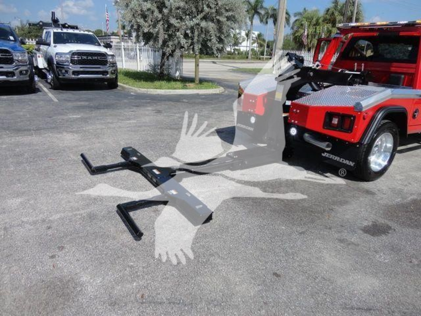 Truck bed winch system and Ram 4500 SLT pickup in a dealership lot; red winch-equipped vehicle on the right, black tow hooks and mounting brackets laid on pavement, other trucks in background.