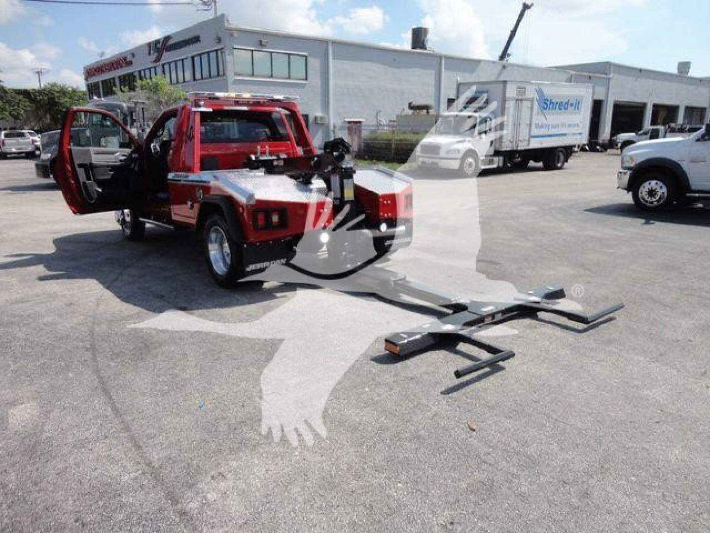 Red Ram 4500 truck with open doors and a visible winch apparatus in a dealership lot. The truck bed and ramp are extended; other vehicles and a building are in the background.