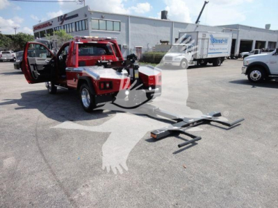 Red Ram 4500 truck with open doors and a visible winch apparatus in a dealership lot. The truck bed and ramp are extended; other vehicles and a building are in the background.