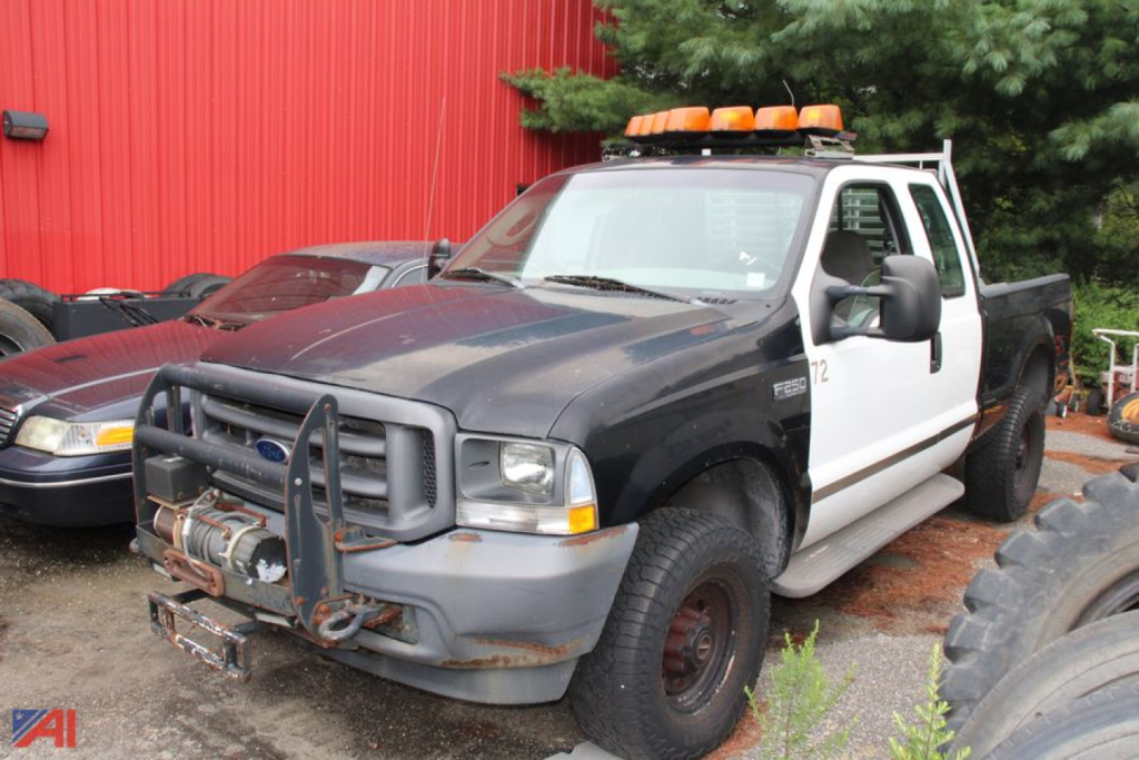 2004 Ford F-250 Super Duty pickup truck with white cab and black body, front grille guard, roof-mounted orange警 lights, tow hitch, and large tires.