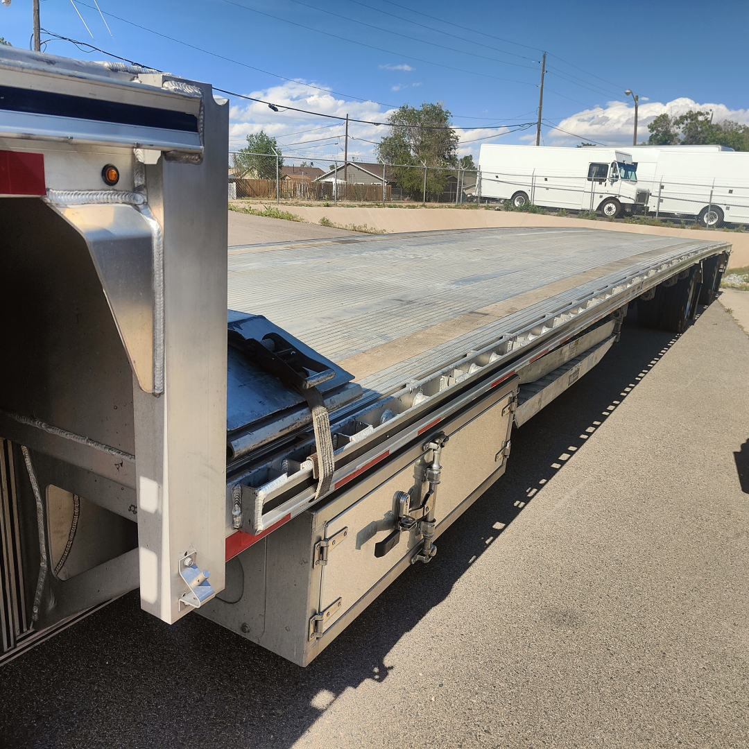 Drop deck trailer showing aluminum platform and rear section with latching mechanisms and side rails.