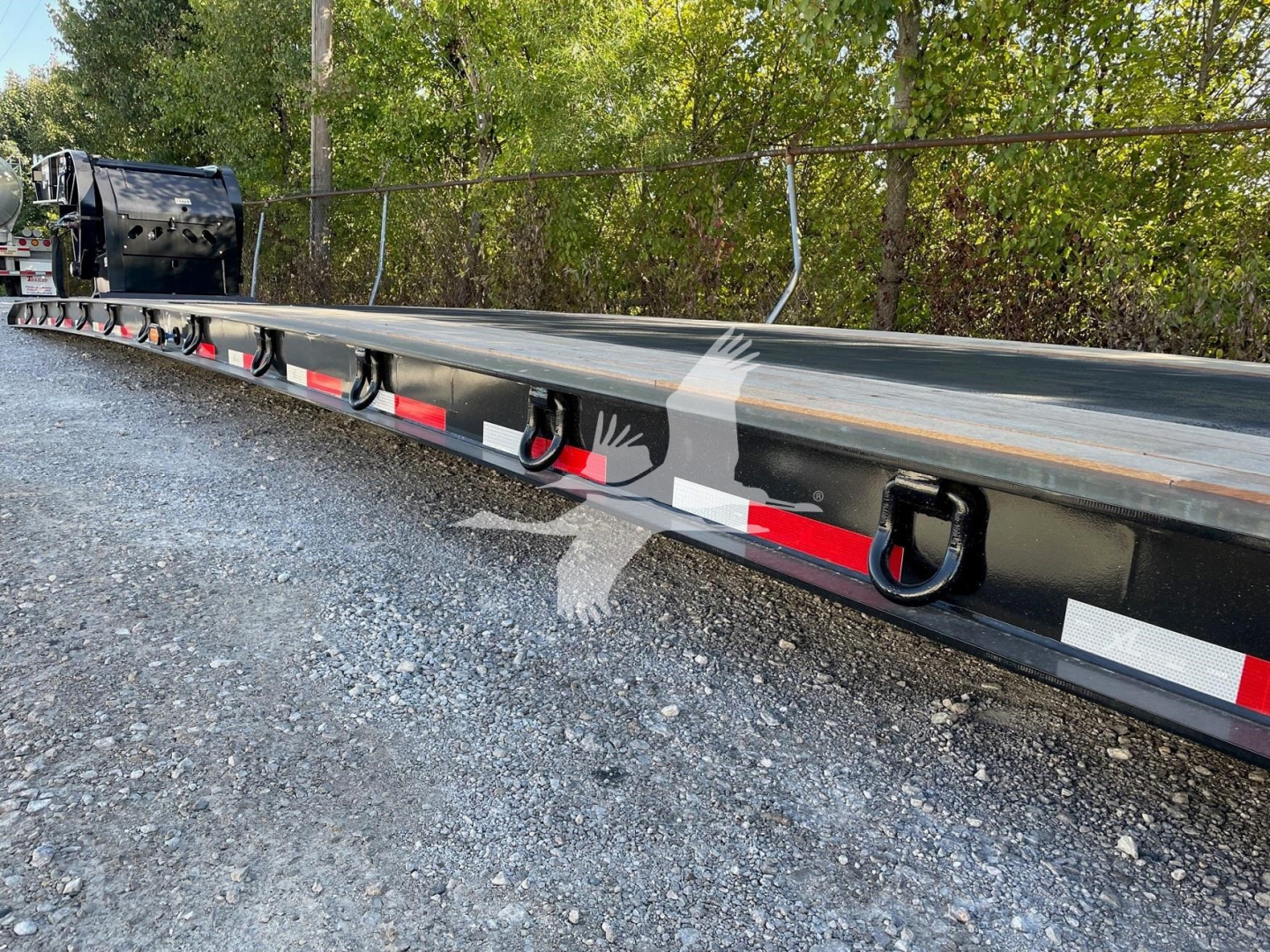 Double drop expandable trailer rail with tie-down rings and reflective red/white safety stripes. Side text and VIN partially visible on the trailer.