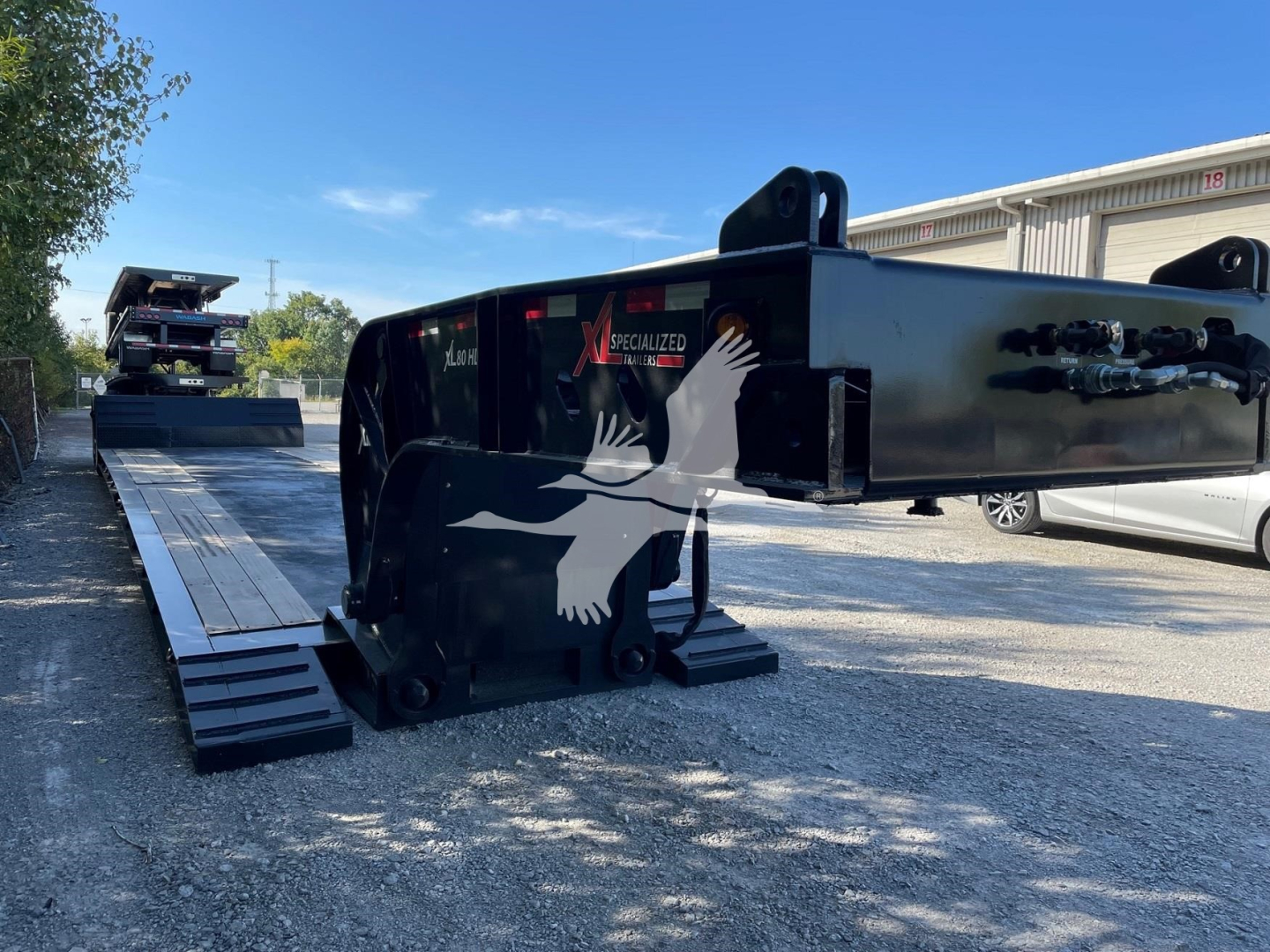 Trailer with a black finish showing a white bird graphic and the text 'XL SPECIALIZED' on the side, plus a long extendable ramp and hydraulic components.