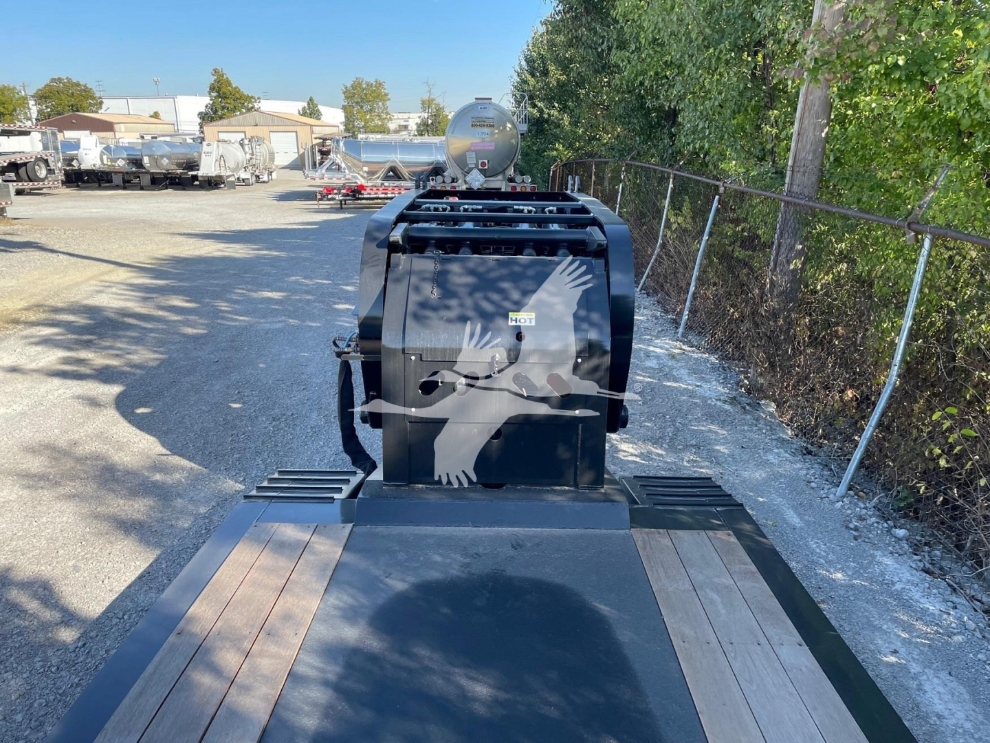 Trailer deck with hydraulic system and control area, black with metal steps on sides and wooden deck, ID plate visible on center hardware.