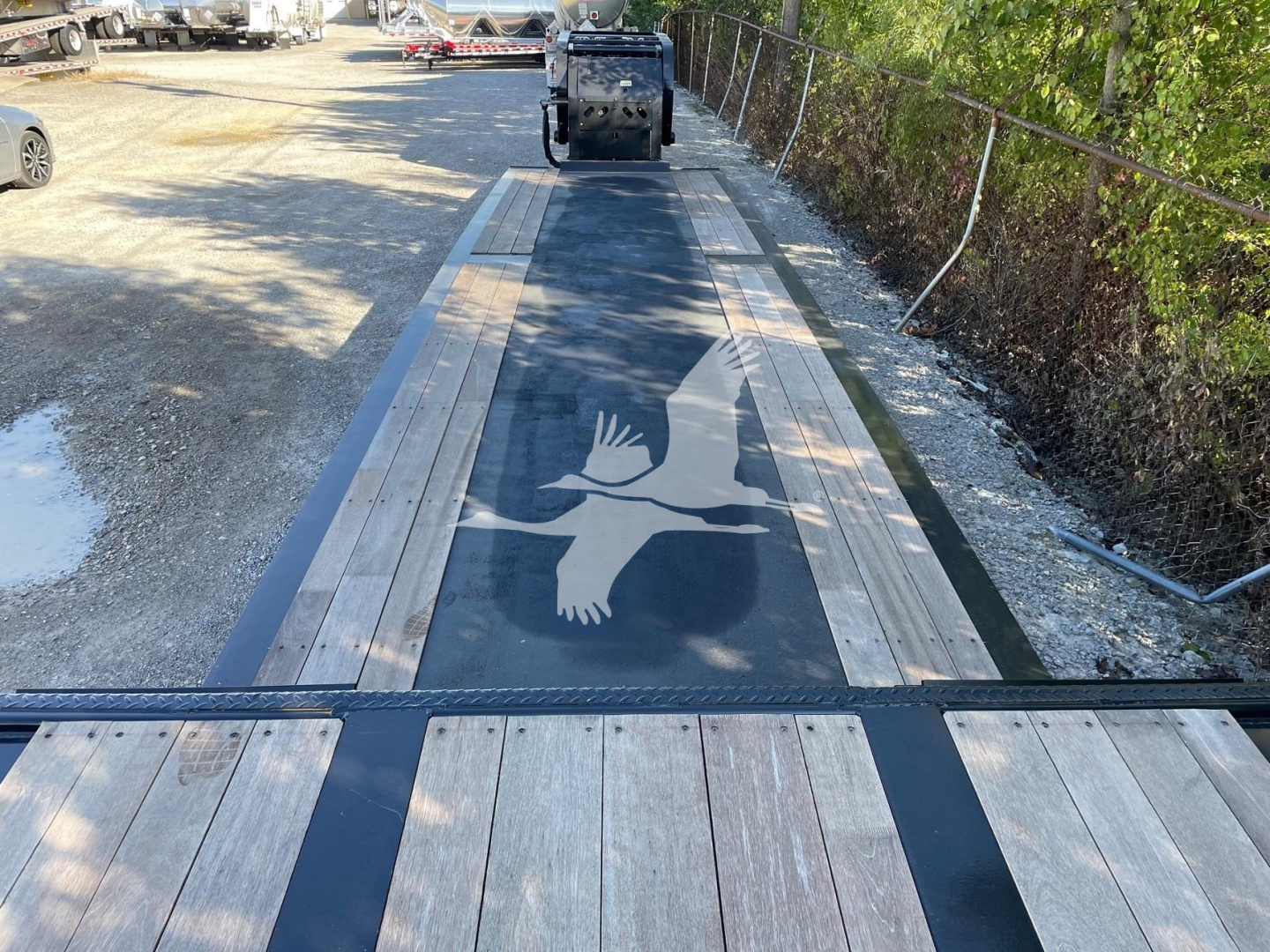 Trailer deck view with long black center stripe and wooden planks on sides, metal frames, and a decal of a bird in flight on the deck.