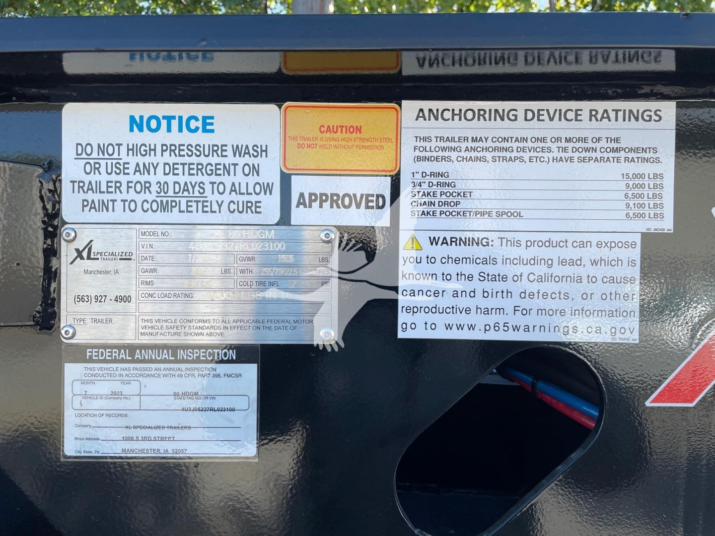 Trailer labeling with notices and ratings, including anchors, warnings, and inspection sticker, on a double drop expandable trailer.
