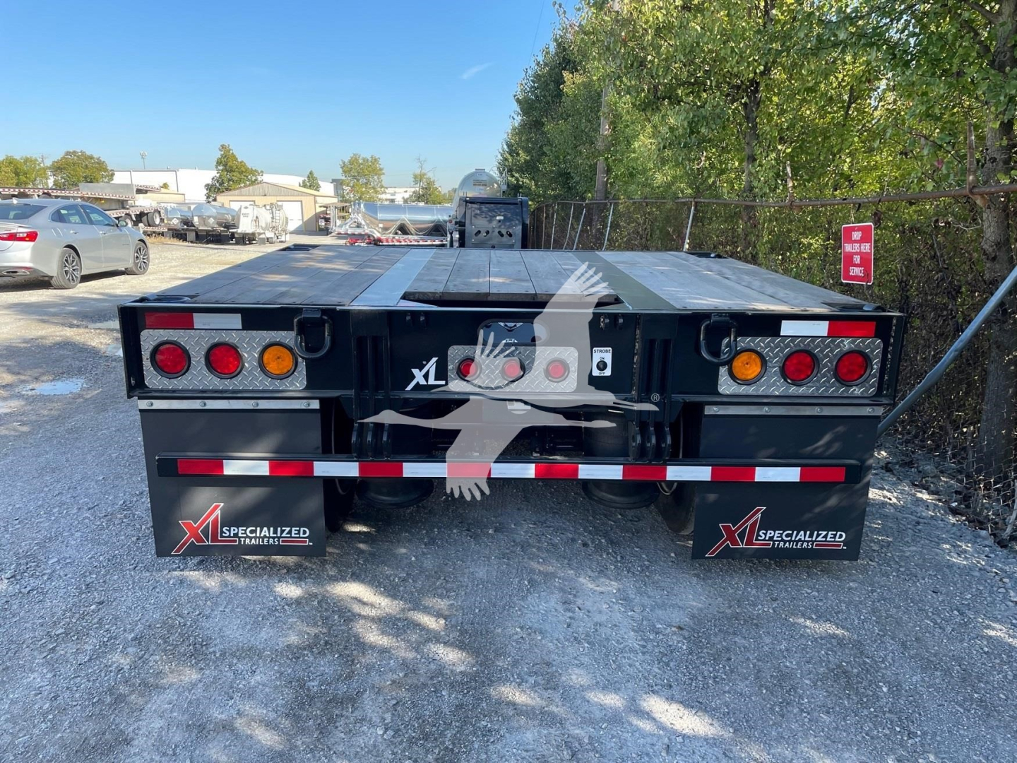 Rear view of a used XL Specialized Mini Deck trailer with dual rear lights, black finish, XLI Specialized Trailers mud flaps, red and white reflective strip, and VIN/stock on labeling
