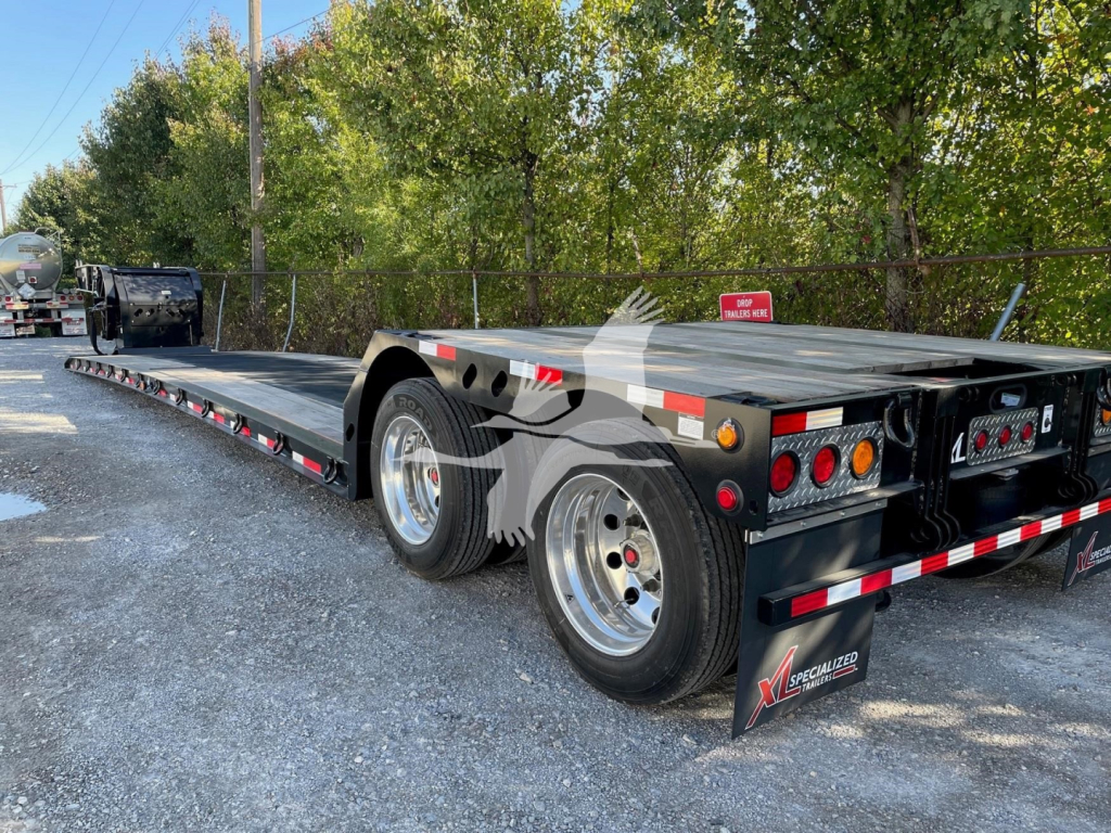 Trailer showing dual tandem axle flatbed with black deck and rear ramps, long extendable deck, and red/white safety markings.