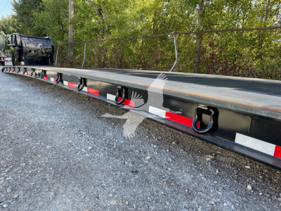 Double drop expandable trailer rail with tie-down rings and reflective red/white safety stripes. Side text and VIN partially visible on the trailer.